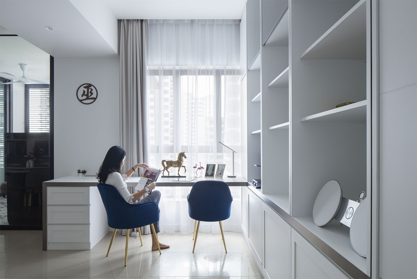 Minimalist white and blue theme study area with white cabinet and racks, white study table and bold blue color chair, gold statue structure, and hidden curtain