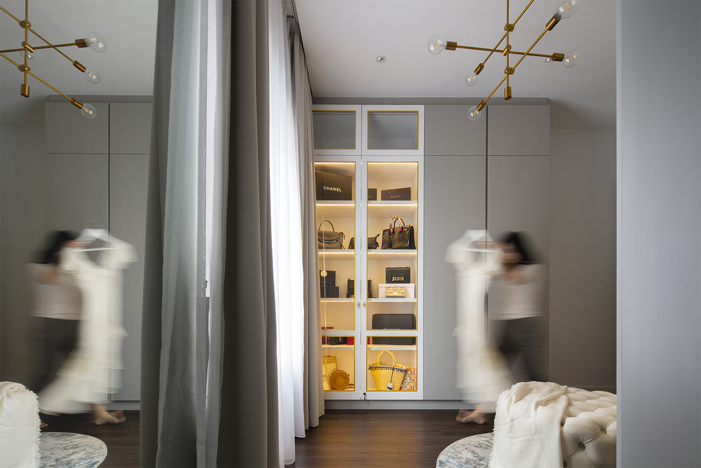Modern walk in closet with glass handbag storage, and gold chandelier