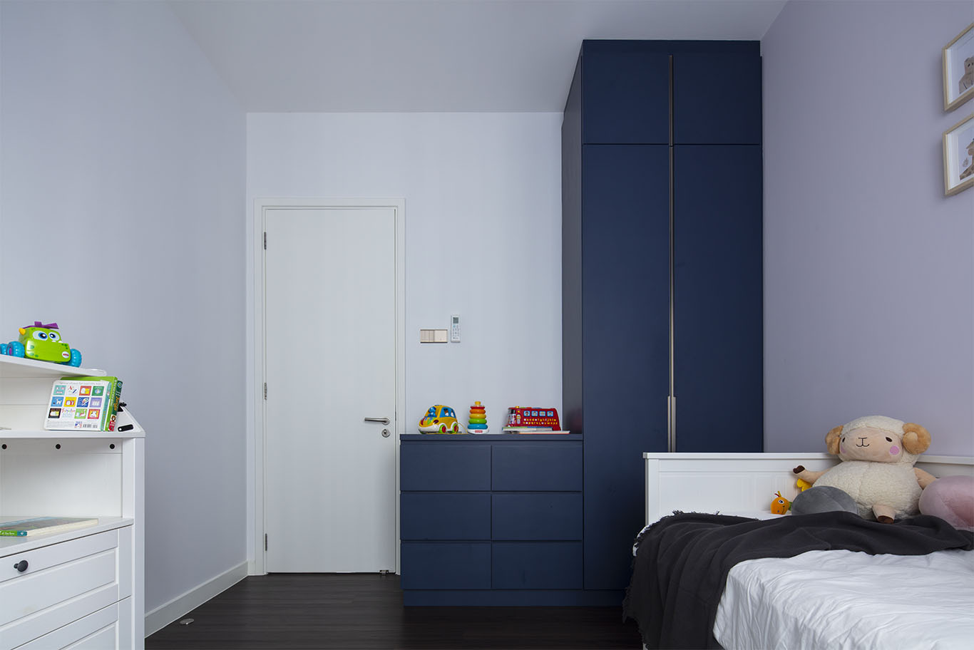 Modern minimalist kids bedroom with wooden floor, white wall, white drawer, white bed, bold blue color cupboard, and colorful toys