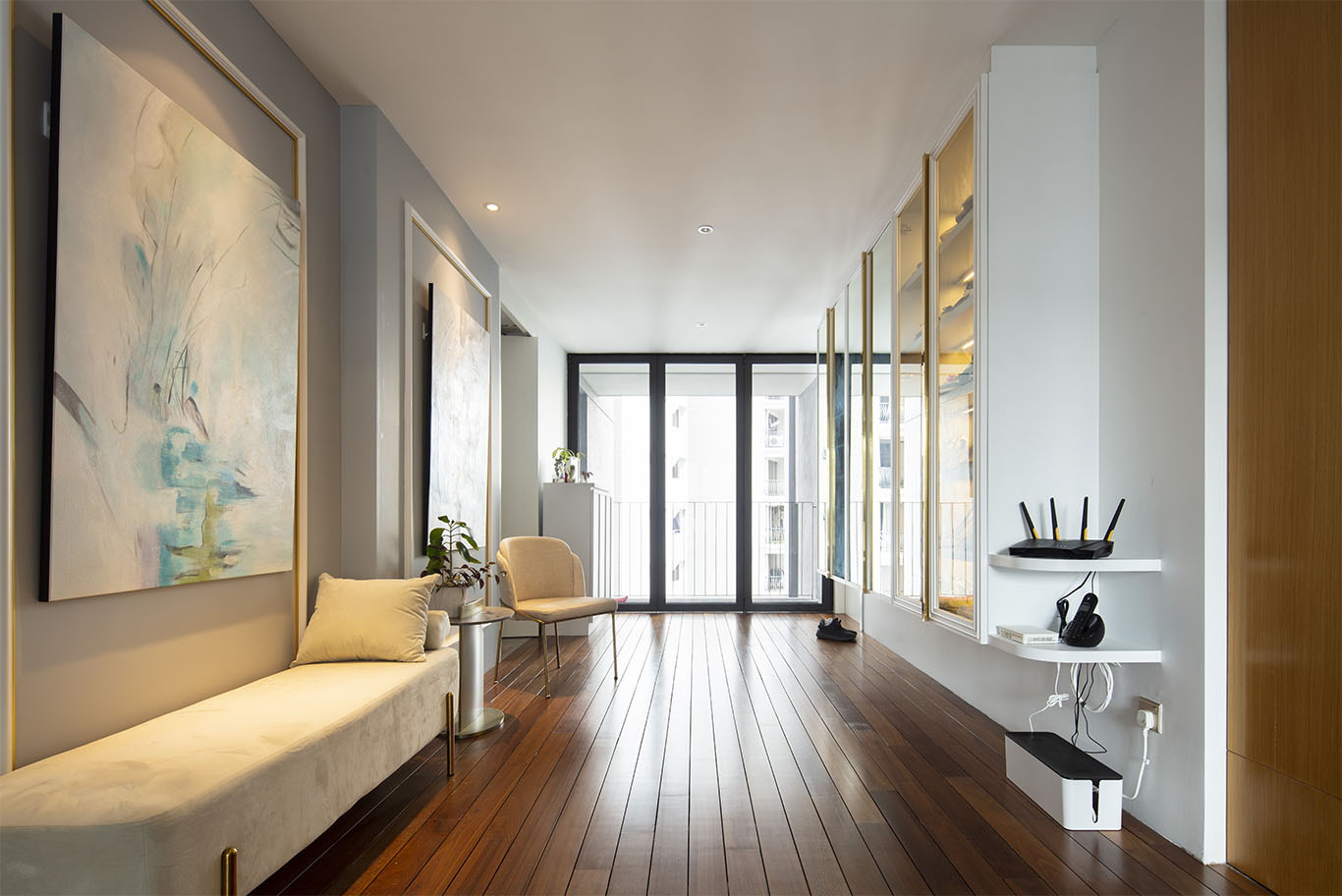 Modern hallway with wooden floor, long velvet chair, modern art display, and glass sliding door