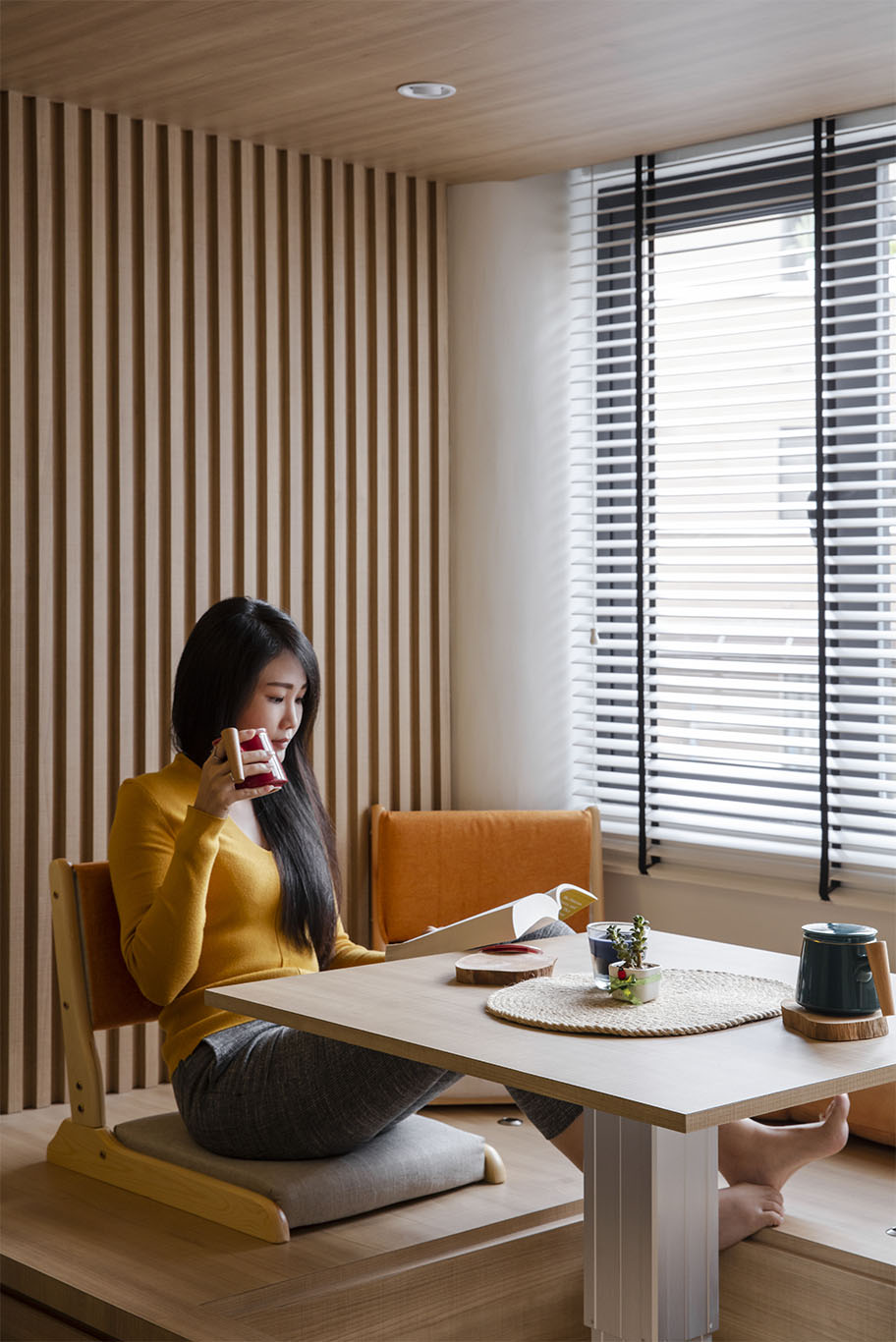 Modern Japanese theme window seat design with wooden strips wall, wooden ceiling with built in minimalist round lamp, minimalist white window blinds, adjustable table, and Japanese chair