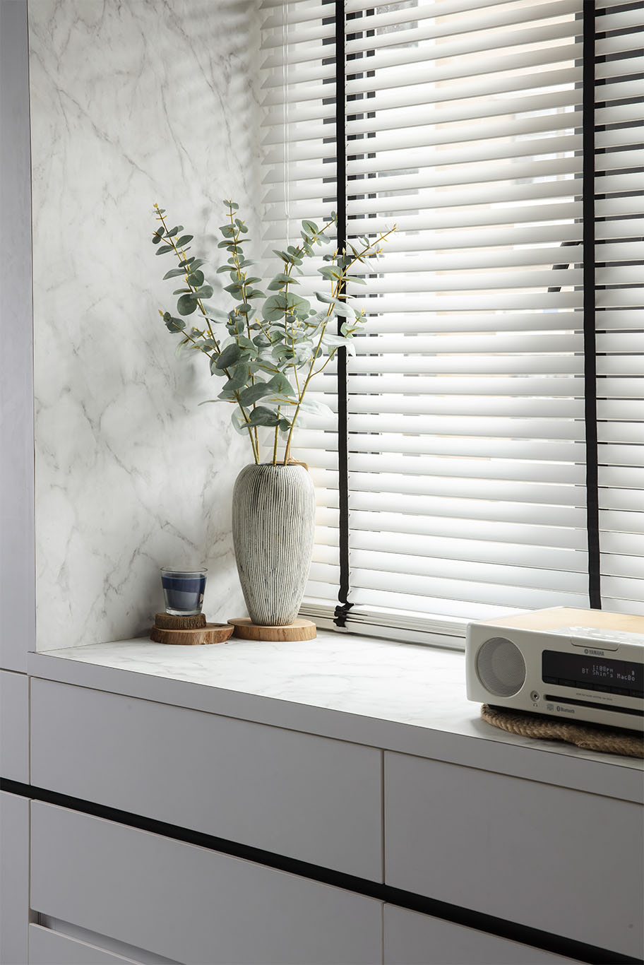 Minimalist decoration with minimalist white window blinds, white cabinet with white marble, white retro radio, and dusty green leaves decoration with minimalist vase